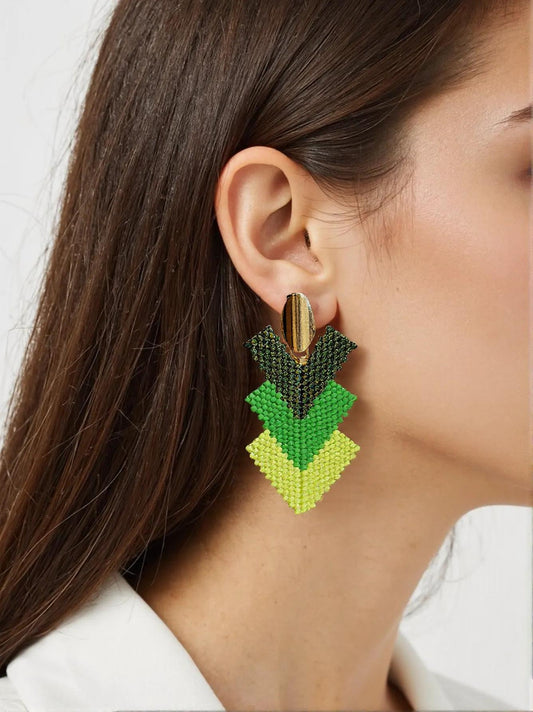 Model med håndlavede øreringe i grønne nuancer og gyldent ophæng – vævede Miyuki-perler i geometrisk diamantmønster