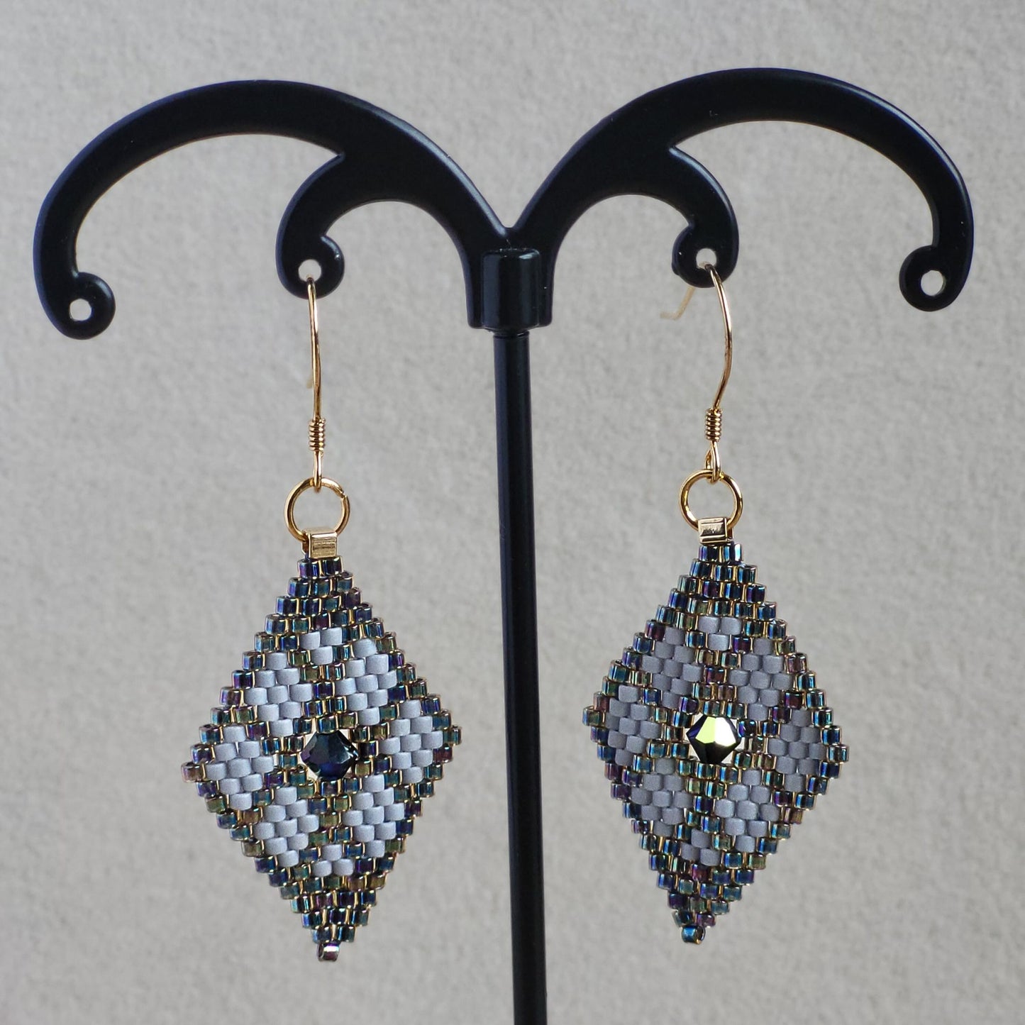 Små håndvævede diamantformede øreringe i grå og solv nuancer – elegante Miyuki-perler i geometrisk mønster med diskret glans