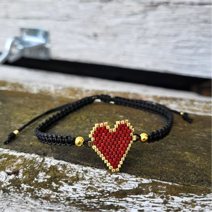 Sort armbånd med rødt hjerte lavet af Miyuki-perler, gulddetaljer og justerbar lukning i macramé – håndlavet og fyldt med personlighed.